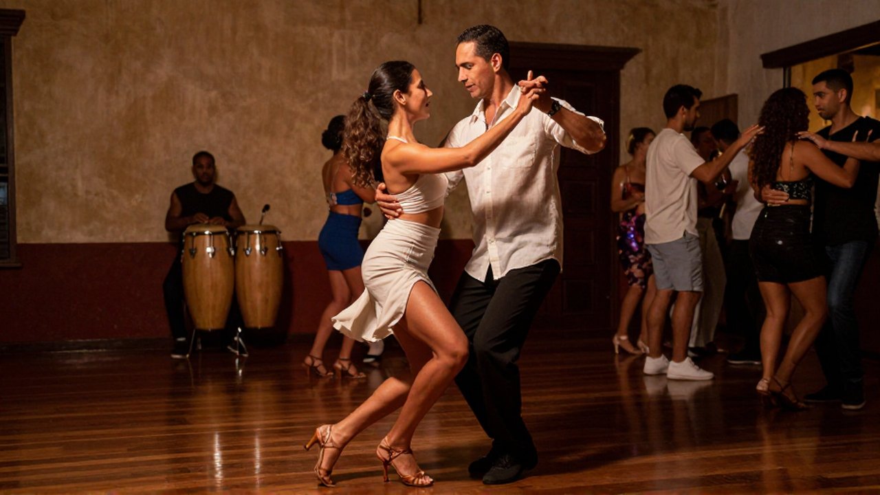 A man and woman in linen clothing perform rhythmic salsa steps in a dimly lit dance hall.